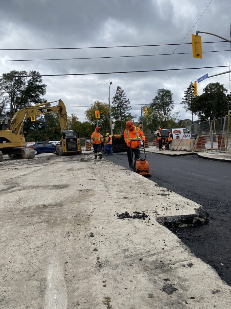 Construction workers in safety gear operating machinery on asphalt paving project, showcasing Strada Paving's commercial maintenance services in Toronto.