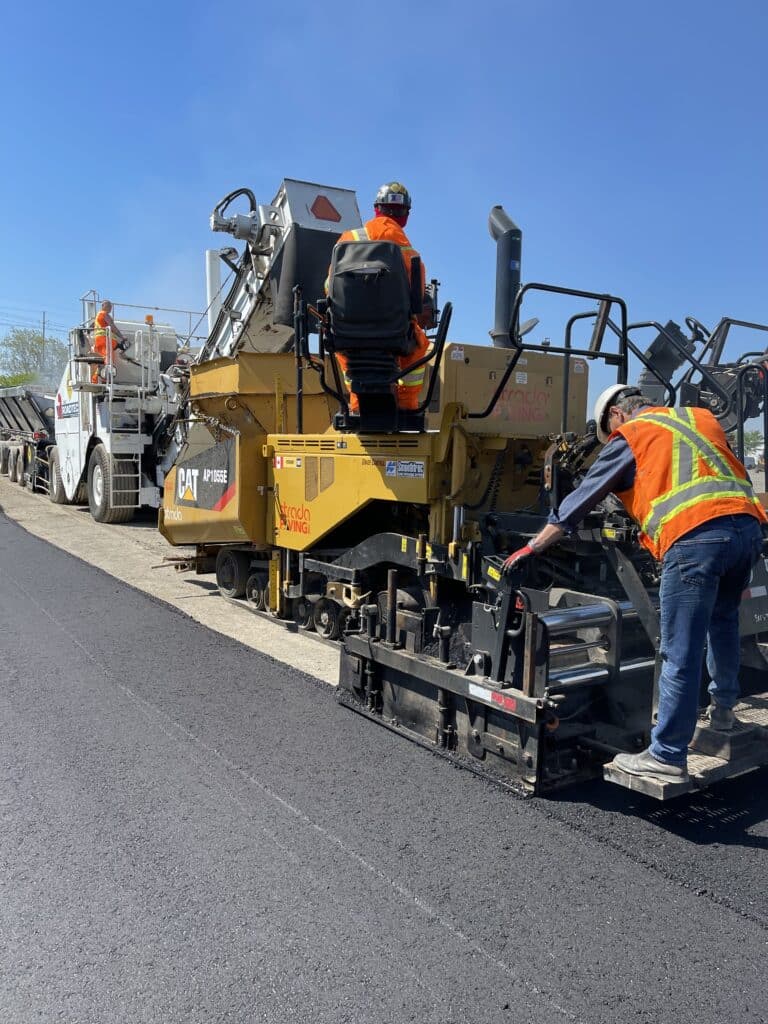 Asphalt paving crew operating heavy machinery on a road project, showcasing Strada Paving's expertise in commercial maintenance services.