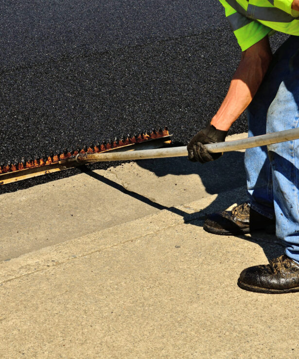 Worker applying asphalt with a screed tool, showcasing paving techniques relevant to Strada Paving's services in asphalt repair and road construction.