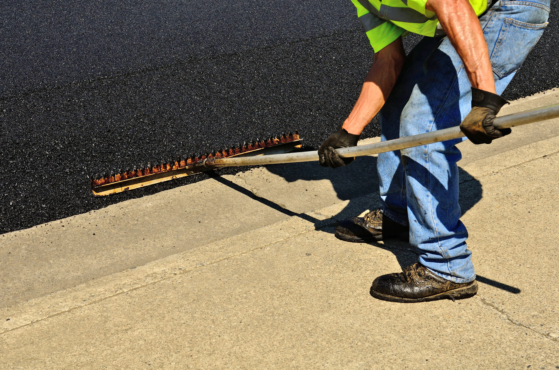 Worker applying fresh asphalt with a long-handled tool on a pavement surface, showcasing professional asphalt repair services.