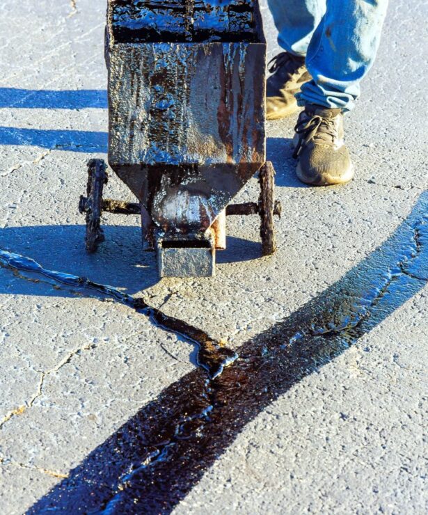 Asphalt crack filling process with worker using a crack sealing machine on a paved surface, showcasing Strada Paving's specialized services for maintaining roadways and driveways.