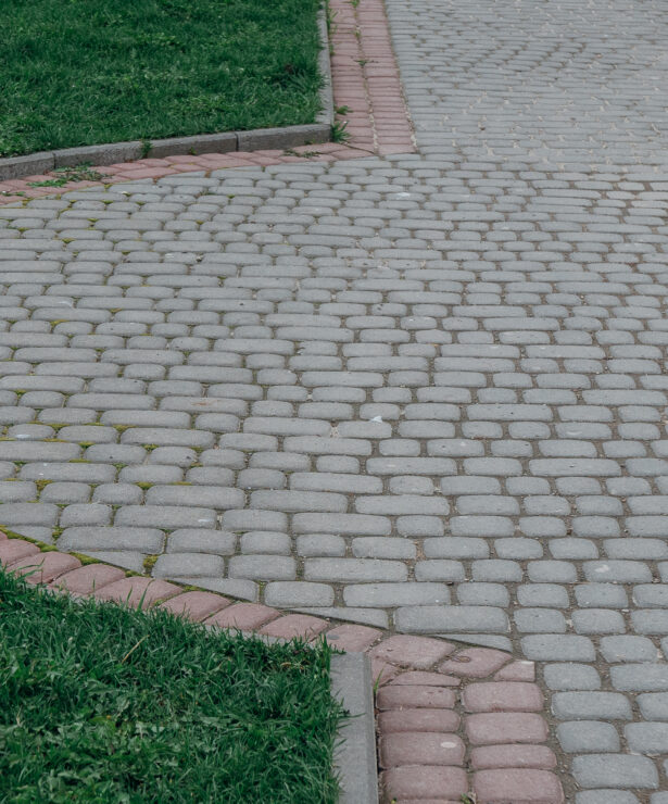 Interlock paving pathway with curved edging and contrasting border bricks surrounded by green grass.