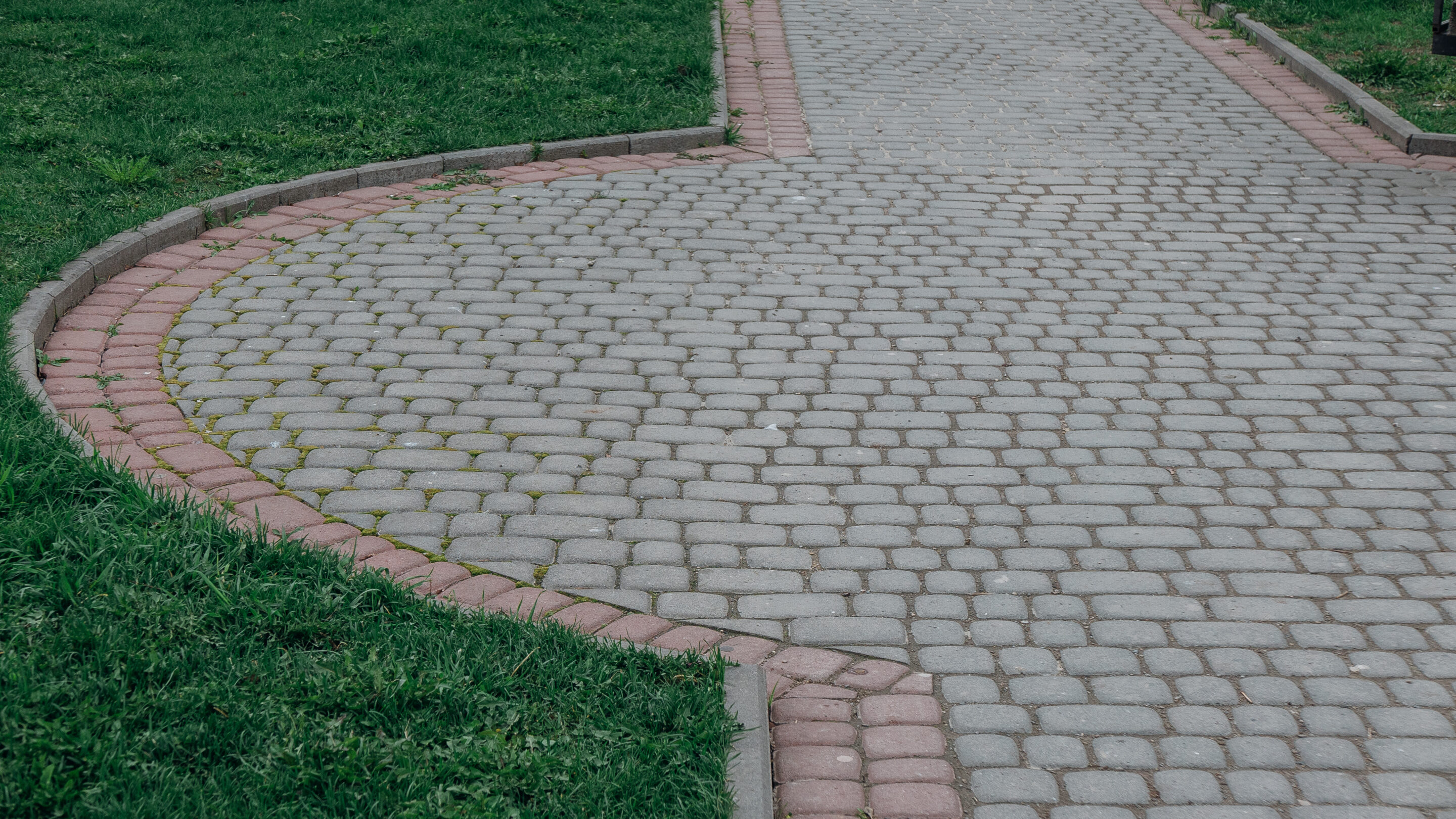 Interlock paving pathway with curved edging and contrasting border bricks surrounded by green grass.
